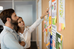 Two employees in front of bulletin board pointing at a posting.
