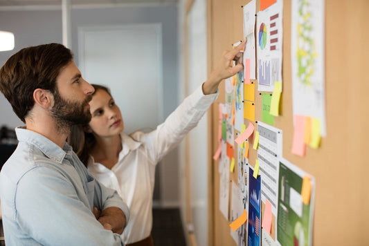 Two employees in front of bulletin board pointing at a posting.