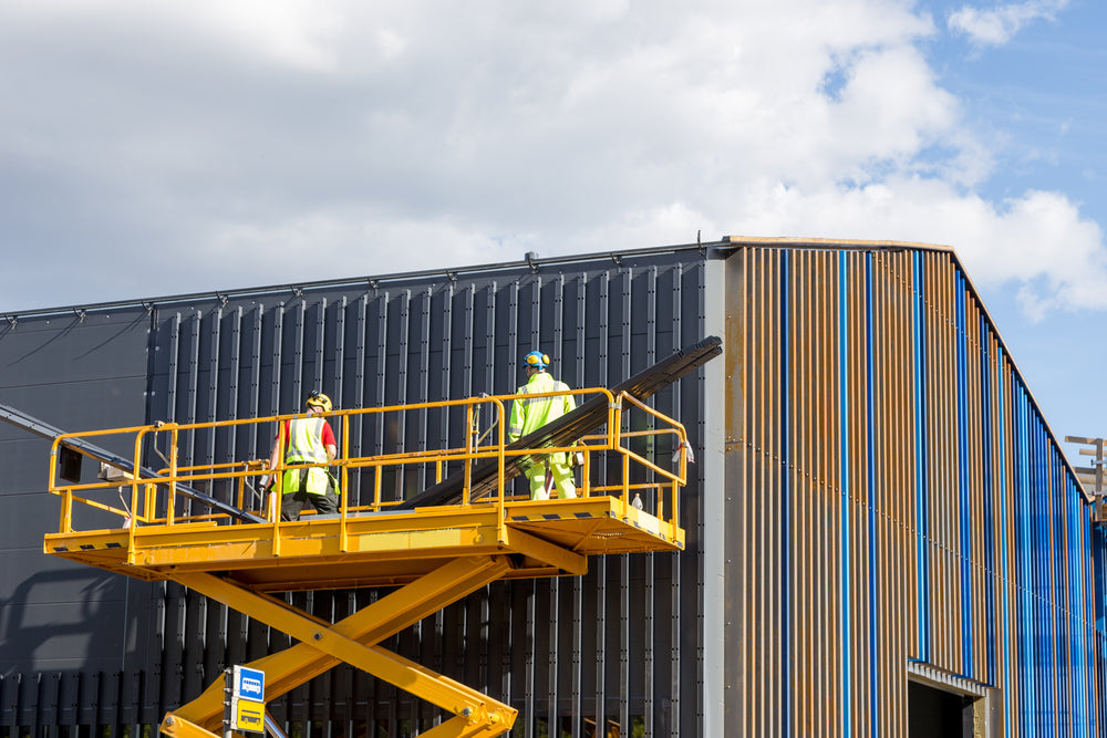 Workers wearing safety gear on a scissor lift platform performing maintenance on a commercial building exterior