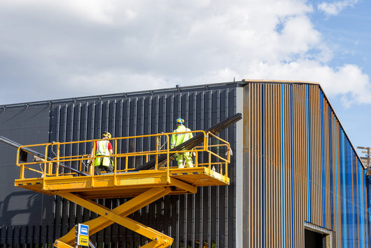 Workers wearing safety gear on a scissor lift platform performing maintenance on a commercial building exterior