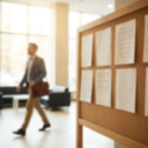 Man walking in an office in background with briefcase and bulletin board out of focus in foreground.