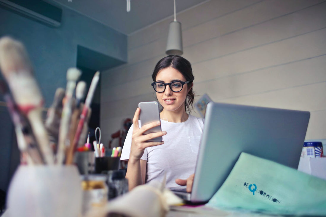 employee sitting at desk with phone in hand and laptop in front of her