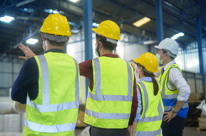 Group of four workers wearing vest and hard hats standing in warehouse and discussing safety