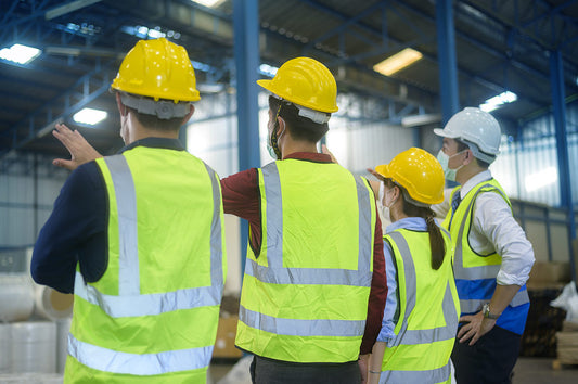 Group of four workers wearing vest and hard hats standing in warehouse and discussing safety
