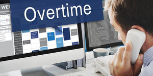 Man in office on phone with Overtime on computer monitor.