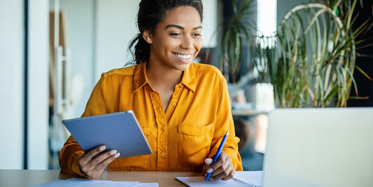 Smiling employee at desk with pen and paper in hand and computer in front of her.
